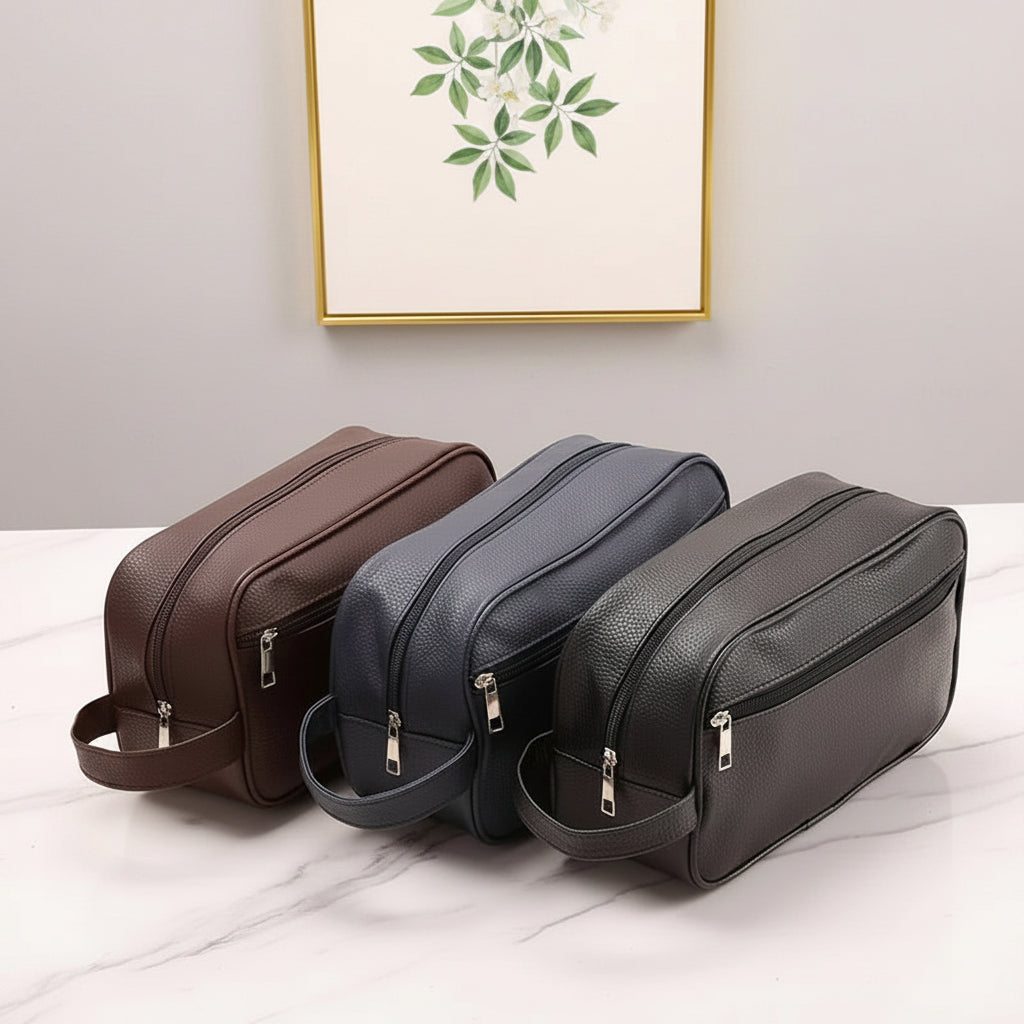 Three leather toiletry bags in brown, blue, and black on a beige surface.